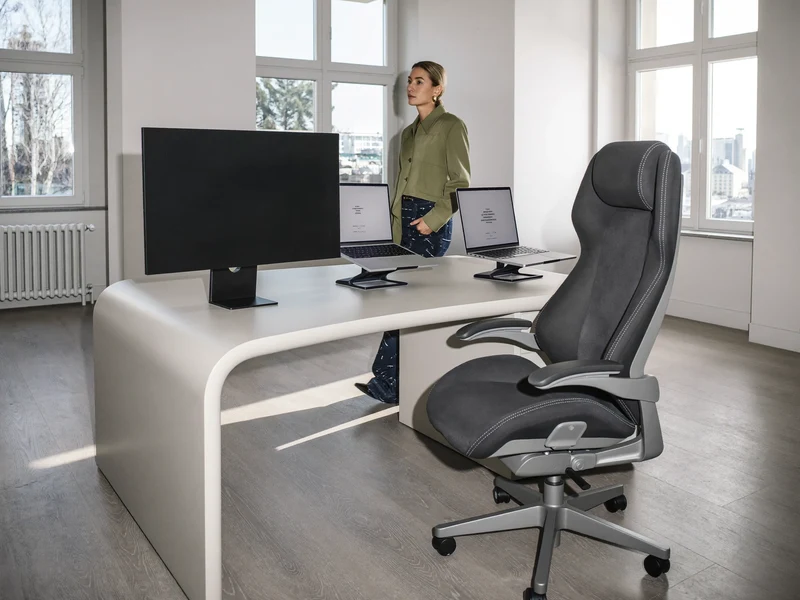 Helle Computerarbeitsstelle mit Stehpult, ergonomischem Stuhl und dunklem Bildschirm im Seitenlicht